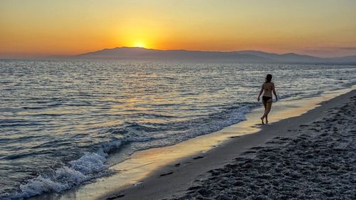 Woman walking on beach against sky during sunset