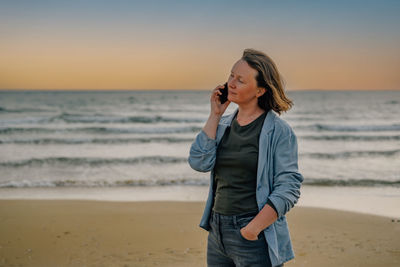 Young woman standing at beach against sky during sunset