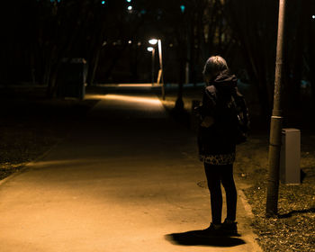 Rear view of woman standing on footpath at night