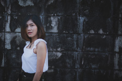 Portrait of young woman standing against wall