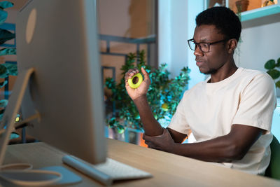 Black guy male freelancer exercising with silicone grip ring or hand expander at cozy home office