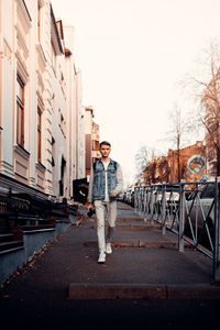 Full length portrait of young man standing against sky in city