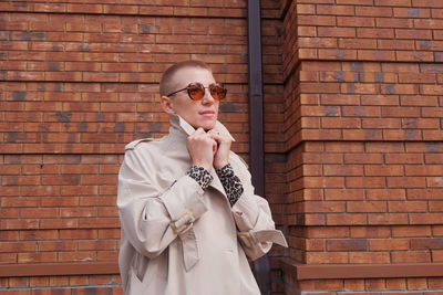 Portrait of man wearing sunglasses standing against brick wall