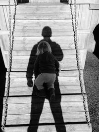 Shadow of man over boy kneeling on footbridge