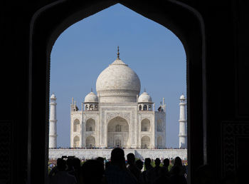 Taj mahal viewed through entrance gate and silhouette of people going through entry gate.