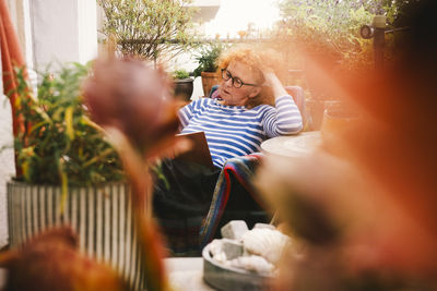 Senior woman reading book while sitting in chair at balcony