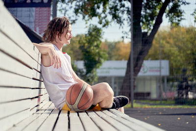 Portrait of young woman sitting on bench in park