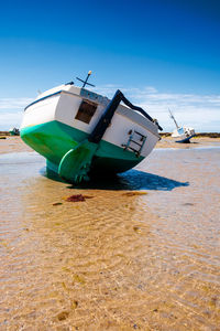 Boat resting on sand at lowtide in summertime surround with clear water and boats in the background