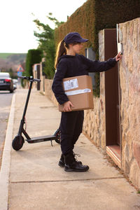 Full length of delivery person holding parcel standing on footpath