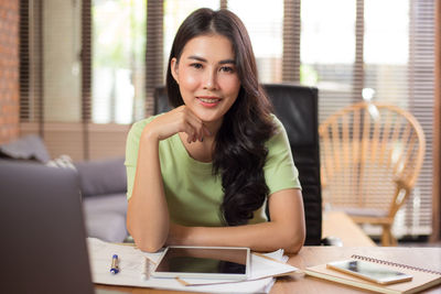 Portrait of young woman using phone while sitting on table