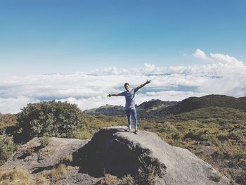 Man with arms outstretched standing on rock against sky