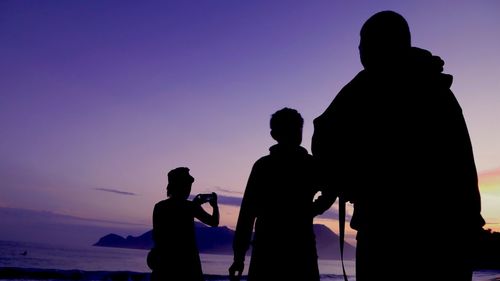 Silhouette man photographing on beach against sky during sunset