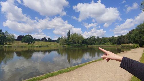 Person hand by lake against sky