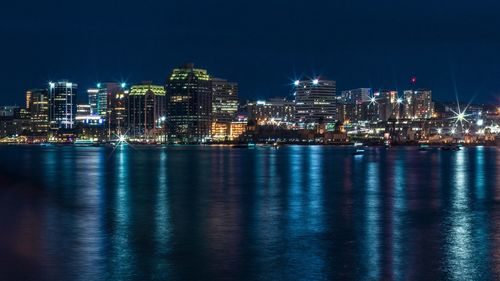 Illuminated buildings by sea against sky at night