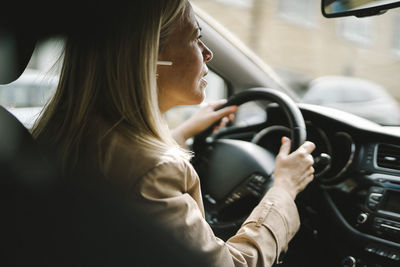 Curious businesswoman with in-ear headphones driving car