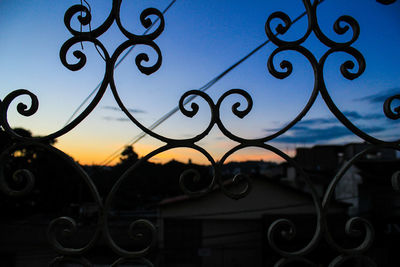 Close-up of metal fence against sunset sky