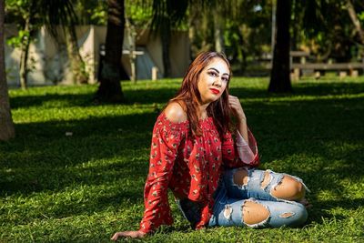 Portrait of woman sitting on grass against trees