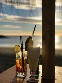 Close-up of beer at beach against sky during sunset