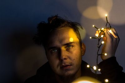 Portrait of young man holding illuminated string lights at night