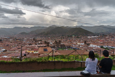 Rear view of man and woman looking at cityscape against cloudy sky