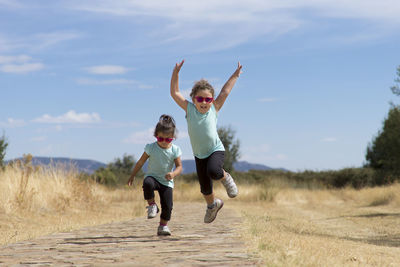 Full length of happy girl jumping on field against sky