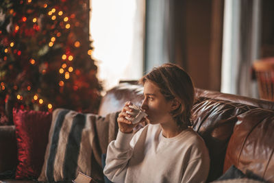 Portrait of candid authentic smiling handsome boy teenager using mobile phone at xmas home interior