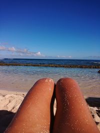 Low section of woman on beach against blue sky