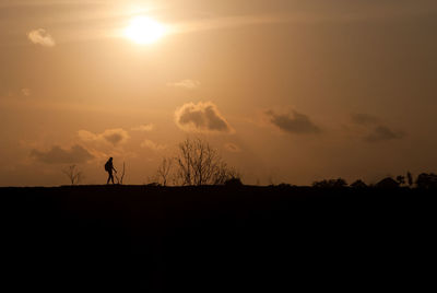 Silhouette man walking on landscape against sky during sunset