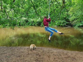 Young woman sitting on rope swing by pond