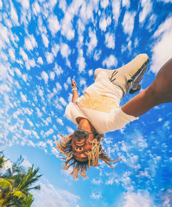 Low angle view of woman holding hands against blue sky