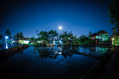 Houses by puddle against sky at night