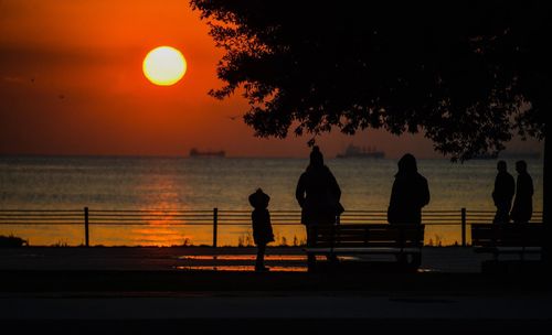 Silhouette people against sea during sunset