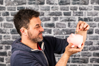 Man holds a piggy bank in his hand against a stone wall