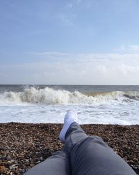 Low section of man at beach against sky