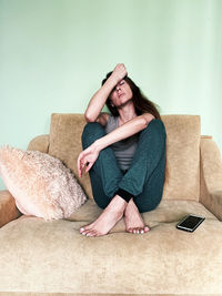 Full length of woman sitting on sofa at home