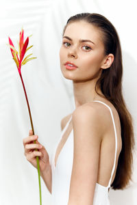 Portrait of young woman holding flower against white background