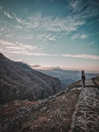 Rear view of man walking on mountain against sky during sunset