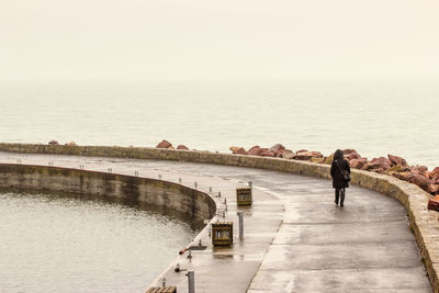 Woman walking on pathway by calm sea