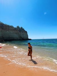 Rear view of woman standing at beach against sky