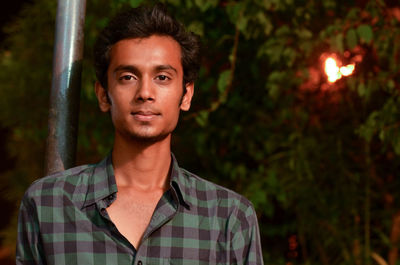 Portrait of young man standing against trees at night