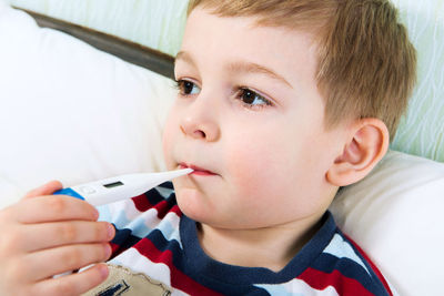 Cute boy holding thermometer in mouth at home