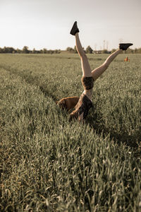 Woman doing handstand by dog on grassy field