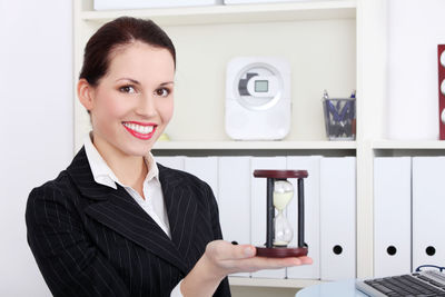 Portrait of smiling young businesswoman holding hourglass
