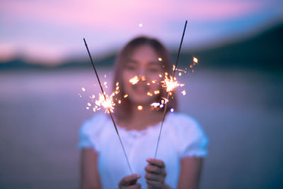 Portrait of woman holding sparkler against sky