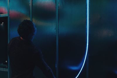 Rear view of man looking at illuminated wall