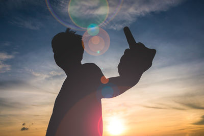 Silhouette man showing obscene gesture against sky during sunset