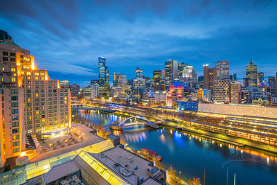 Illuminated buildings by river against sky in city at night