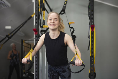 Portrait of happy young woman leaning on gymnastics rings at health club