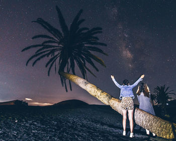 Low angle view of woman with arms outstretched standing against sky at night