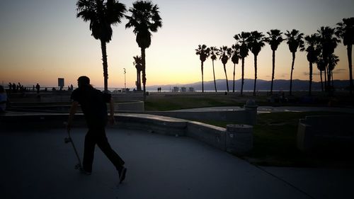 Silhouette man standing by sea on a skateboard against sky during sunset
